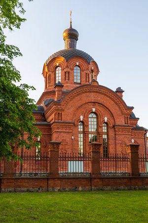 A red brick Orthodox church with decorative towers and domes stands behind a fence in Bialowieza, Poland, at sunset.の写真素材