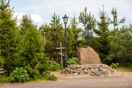 Orthodox metal cross mounted on a large stone surrounded by trees and pathway in Odrynki, Poland.の写真素材