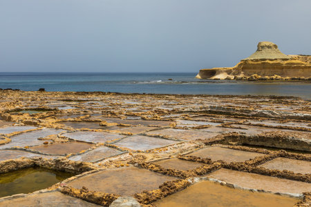 Traditional salt pans on the rocky coast of Gozo Malta with limestone cliffs in the background.の写真素材
