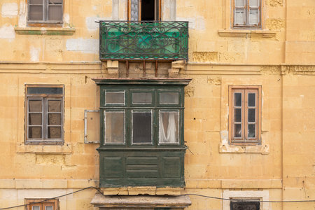 Traditional Maltese wooden balcony with peeling paint and surrounding windows on an old limestone building in Valletta, Malta.の写真素材