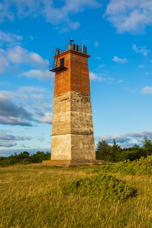 A historic red and white lighthouse tower stands on a grassy coastal field on Saaremaa island, Estonia.の写真素材