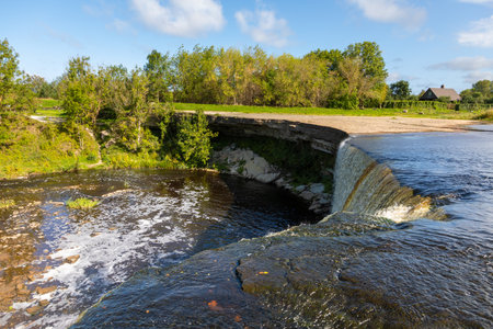 Wide curtain-style waterfall flowing over a rocky edge into a river pool in Lahemaa National Park, Estonia.の写真素材