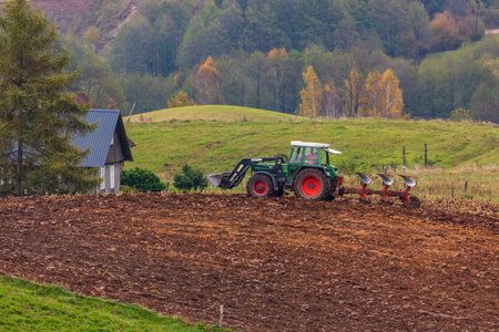 Podlasie, SuwaÅki Landscape Park, Poland â 15 Oct 2021. A tractor plows a rural field among rolling hills and autumn trees.のeditorial素材