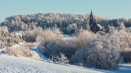Snow-covered fields and a winding road leading toward the church in Wygoda Åaczynska, Poland, on a clear winter morning.の写真素材