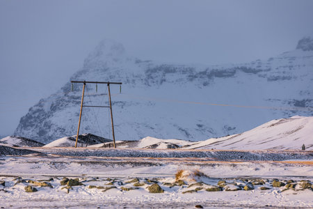 Wooden power poles standing in a snowy landscape near the Jokulsarlon Glacier Lagoon in Iceland, with distant mountains covered in winter light.の写真素材