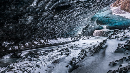 Inside the Blue Ice Cave of Vatnajokull National Park in Iceland, the sculpted glacial ceiling reveals deep blue ice formations above a snowy.の写真素材