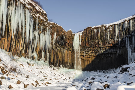 Frozen sections of Magnusarfoss waterfall in Iceland with snow-covered cliffs and winter landscape.