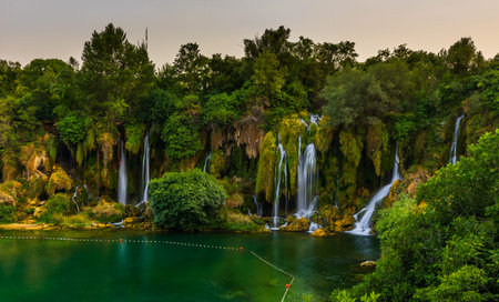 Kravica Waterfalls presenting multiple cascades flowing into a vibrant green river, surrounded by lush vegetation and trees, Bosnia and Herzegovinaの写真素材