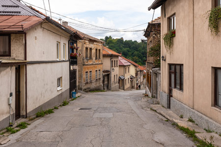 Travnik, Bosnia and Hercegovina - August 24, 2022: Winding old town street descending with aged buildings and green hills.のeditorial素材