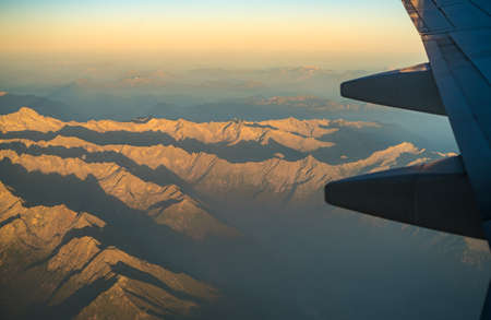 Mountain range seen from Airplane, with plane wing seen on the right side. Mountains during sundown, aerial shot of Mountainsの写真素材