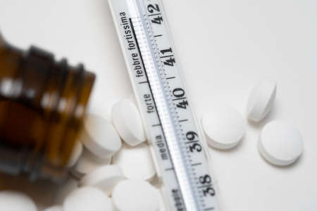 Mercury in glass thermometer on white surface with medicine and pills. Analog fever thermometer and...