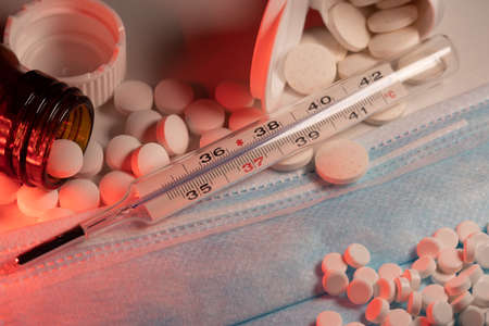 Fever Thermometer on blue face mask. White pills and medicine behinde clinical thermometer. Surgical...