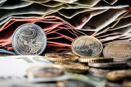 Two, 2, and one, 1, Euro coins in front of a stack of ten euro bills and 5 â¬ banknotes on top. Different coins on bottom out of focus.の写真素材