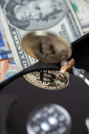 Bitcoin reflecting on hard drive platter. Digital crypto currency on hard disk and dollar banknotes...