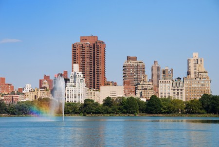 New York City Central Park fountain with rainbow and urban Manhattan skyline with skyscrapers and trees lake reflection with blue sky and white cloud.の写真素材