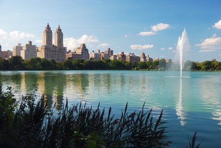New York City Central Park fountain and urban Manhattan skyline with skyscrapers and trees lake reflection with blue sky and white cloud.の写真素材