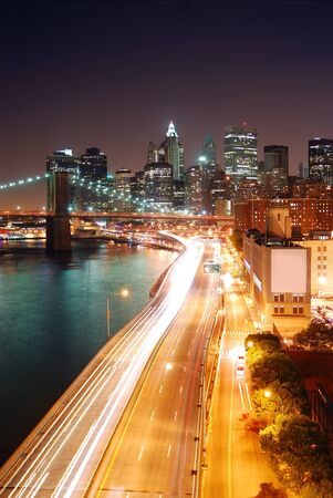 New York City Manhattan skyline and Brooklyn Bridge with skyscrapers over Hudson River illuminated with lights and busy traffic at dusk after sunset.の写真素材