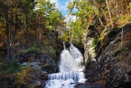 Waterfall in mountain with Autumn foliage and woods over rocks.の写真素材