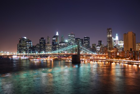 New York City Brooklyn Bridge and Manhattan skyline with skyscrapers over Hudson River illuminated with lights at dusk after sunset.の写真素材