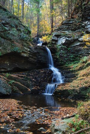 Waterfall in mountain with Autumn foliage and woods over rocks.の写真素材