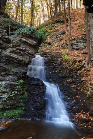 Waterfall in mountain with Autumn foliage and woods over rocks.の写真素材