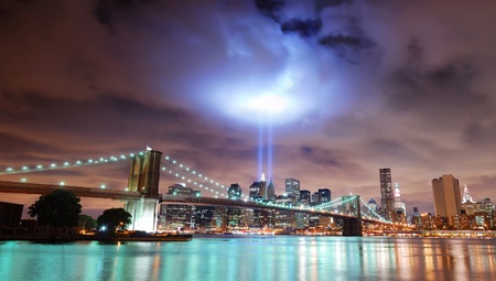 Remember September 11. New York City Manhattan panorama view with Brooklyn Bridge at night with office building skyscrapers skyline illuminated over Hudson River and two light beam in memory of September 11.の写真素材