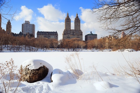 New York City Manhattan Central Park in winter with ice and snow over lake with rocks, skyscrapers and blue cloudy sky at dusk.の写真素材
