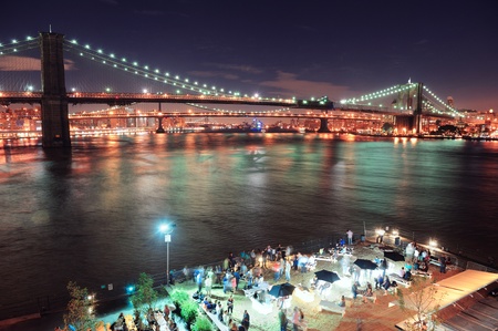 Brooklyn Bridge over East River at night in New York City Manhattan with lights and reflections and people in club bar enjoying the view.のeditorial素材