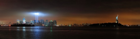 New York City Manhattan downtown skyline at night with statue of liberty and light beams in memory...