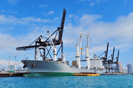 Cargo ship at Miami harbor with crane and blue sky over sea.のeditorial素材
