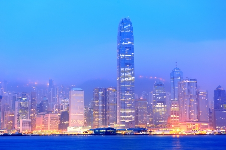Hong Kong Victoria Harbor morning with urban skyscrapers over sea with blue tone and street light.