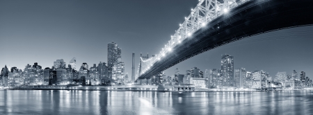 Queensboro Bridge over New York City East River black and white at night with river reflections and midtown Manhattan skyline illuminated. の写真素材