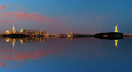 New York City at night with urban architectures reflections and statue of libertyの写真素材