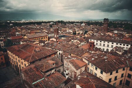 Lucca rooftop view with red roofs of historic buildings and mountain range in Italy.