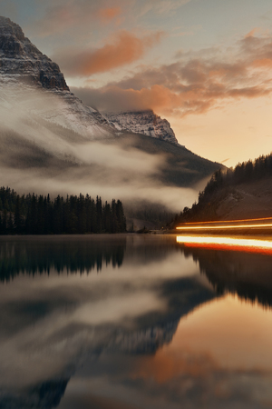 Mountain lake and traffic light trail with reflection and fog at sunset in Banff National Park, Canada.の写真素材