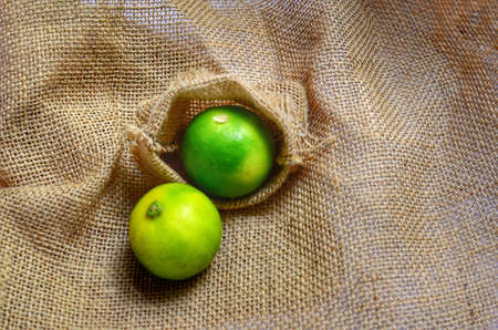 Two fresh citrus fruits organic key limes on burlap fabricの写真素材