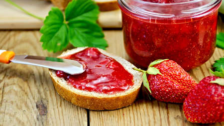 Bread with strawberry jam and chamomile on a wooden board.の写真素材