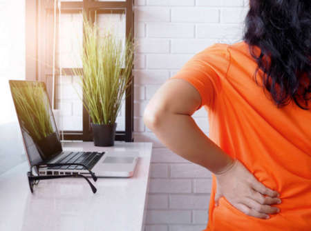 Young asian woman working with laptop computer and sitting on chair and suffering low spine back pain and waist sore, health concept and body aches.の写真素材