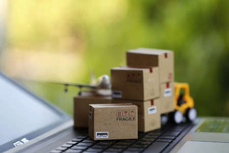 Logistic and cargo freight concept: fork-lift a truck moves a paper box on notebook keyboard in the natural green nature. depicts international freight or shipping service for online shoppingの写真素材