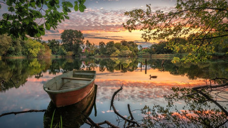 A boat on a lake. The boat is a prominent feature like the lake, including elements like water, sky, landscape, trees, clouds, reflection, and a sunset.の写真素材