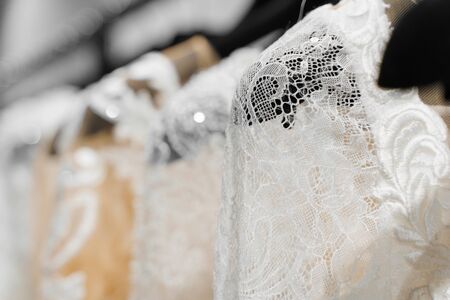 Cloth of wedding dresses made of silk chiffon, tulle and lace. Beautiful White cream bridal dress on hangers in wedding salon. Pearls and crystals pendants on the sleeves of a wedding dressの写真素材