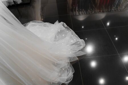 Cloth of wedding dresses made of silk chiffon, tulle and lace. Beautiful White cream bridal dress on hangers in wedding salon. Pearls and crystals pendants on the sleeves of a wedding dressの写真素材