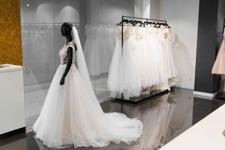Dummy in wedding dress made of silk chiffon, tulle and lace. Interior of wedding shop. White cream bridal dress on hangers in wedding salon. Pearls and crystals pendants on the sleeves.の写真素材