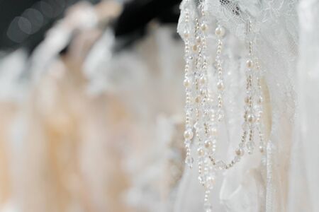 Wedding dresses made of silk chiffon, tulle and lace. Beautiful White cream bridal dress on hangers in wedding salon. Pearls and crystals pendants on the sleeves of a delicate color of a wedding dressの写真素材