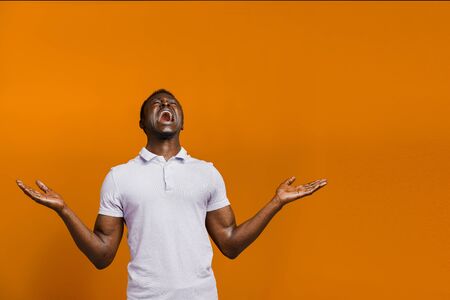 Happy handsome black man wins online bet on orange background. Shouting loud "Yes" and making crazy emotions. African won a prize. Online work at home quarantine concept. Empty right side for advertの写真素材