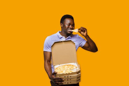 Funny black courier eats piece of pizza and holds 4 pizza boxes. 2+2 Big discount for customers. Tasty food pizza delivery from restaurant. Safety delivery. Pizza with cheese boards advert.の写真素材