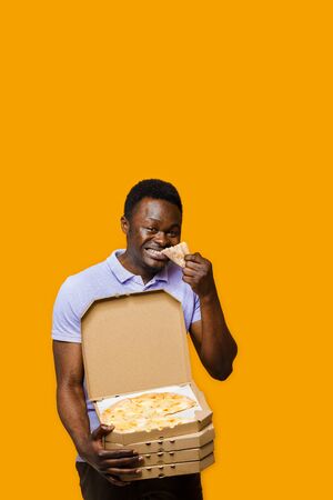 Funny black courier eats piece of pizza and holds 4 pizza boxes. 2+2 Big discount for customers. Tasty food pizza delivery from restaurant. Safety delivery. Pizza with cheese boards advert.の写真素材