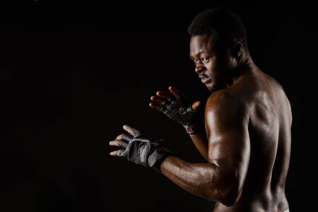 Athletic african fighter on black background. Dark skinned undressed man shows a fight. Advert for sport club and gym. Professional boxing and karateの写真素材