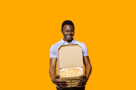 Funny african bearded courier with 4 pizza boxes. 2+2 Big discount for customers. Tasty food pizza delivery from restaurant. Safety delivery. Pizza with cheese boards advert. Isolated yellow background.の写真素材