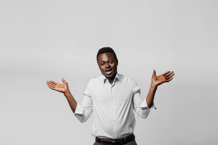 Handsome surprised black man shrugs and gives a choose. Choosing between 2 items. African offers a choice. Dark skinned man advert for business on white backgroundの写真素材